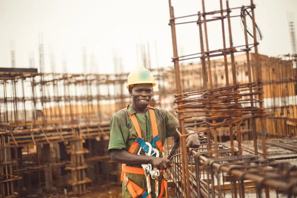 Un ouvrier souriant, casque jaune et harnais, sur un chantier de béton armé
